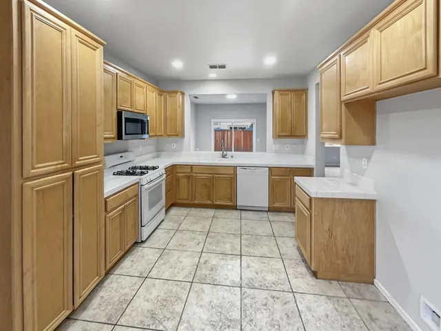 Kitchen with white appliances, tile counters, recessed lighting, and light tile patterned flooring
