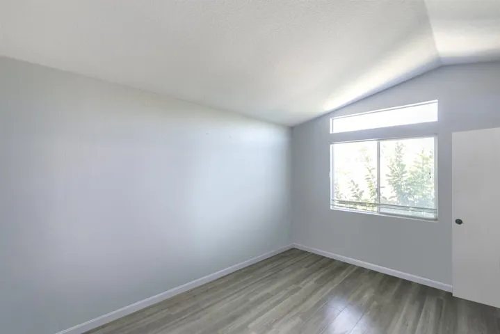 Empty room with lofted ceiling, wood finished floors, and a textured ceiling