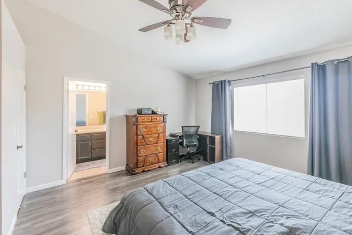 Bedroom featuring lofted ceiling, wood finished floors, a ceiling fan, an office area, and ensuite bathroom