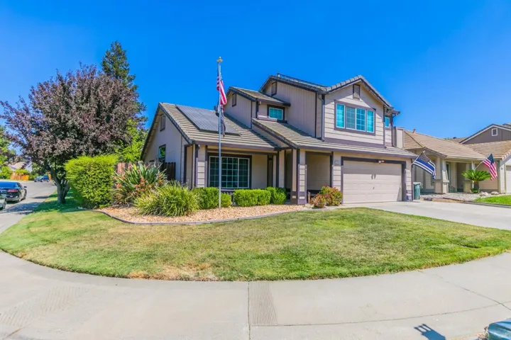 Traditional home featuring a garage, a front lawn, driveway, a tiled roof, and roof mounted solar panels