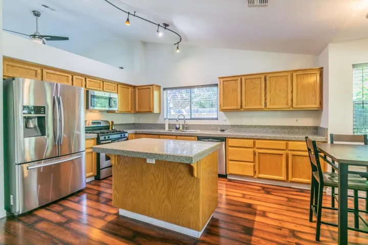 Kitchen featuring appliances with stainless steel finishes, a kitchen island, brown cabinets, dark wood-style floors, and high vaulted ceiling