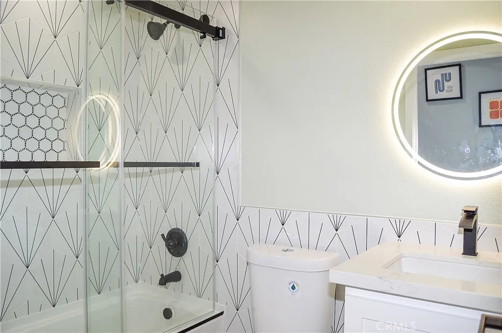 This stunning main floor bath sits across from the 4th bedroom and offers a custom tile surround for the shower/tub combo with sliding glass doors, a lighted mirror over the modern vanity, recessed lighting, tile flooring, and a dual-flush commode.