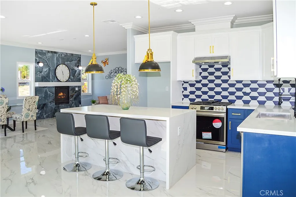 Gorgeous, modern kitchen with two-tone soft-close cabinetry with gold hardware, stainless steel appliances and sink, a quartz-topped breakfast bar with waterfall edges with pendant lighting above it, custom tile backsplash, and recessed lighting - all open to the great room and the views.