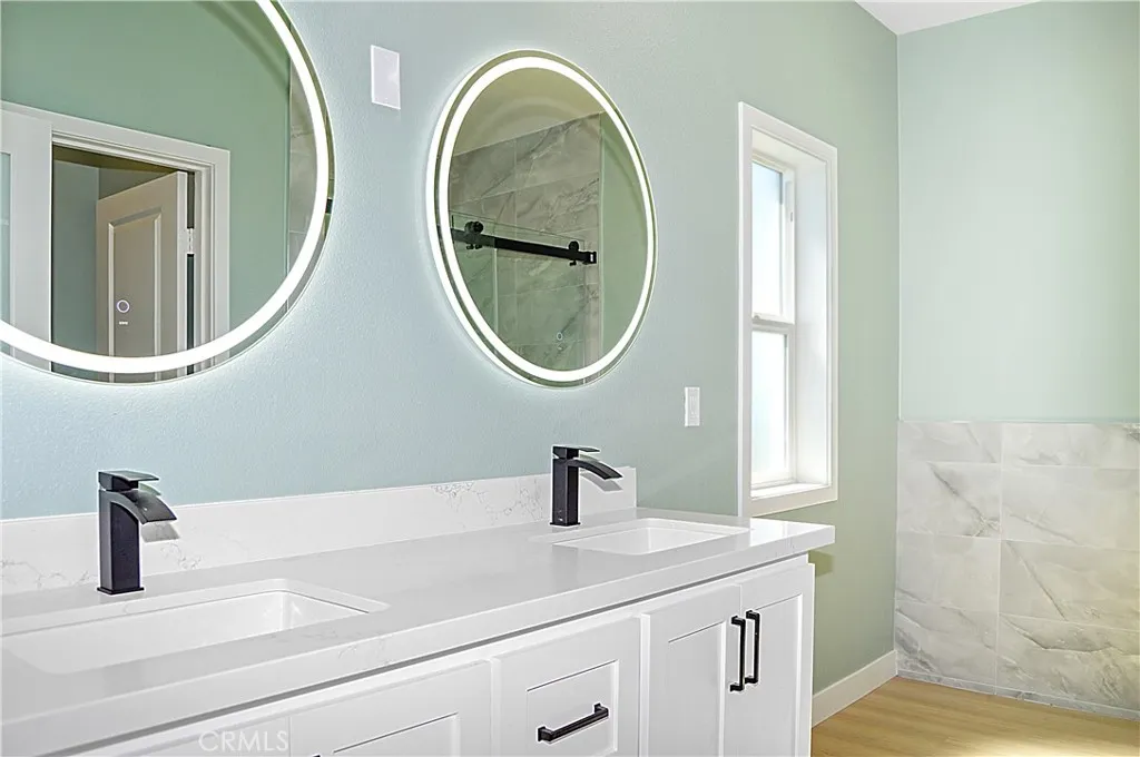 The primary suite's bath is accessed via an opaque glass door and offers dual sinks in the modern vanity, dual lighted mirrors, easy-access walk-in shower with custom tile surround, private toilet room, and recessed lighting