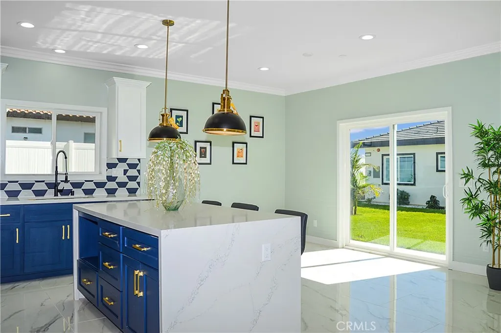 Gorgeous, modern kitchen with two-tone soft-close cabinetry with gold hardware, stainless steel appliances and sink, a quartz-topped breakfast bar with waterfall edges with pendant lighting above it, custom tile backsplash, and recessed lighting - all open to the great room and the views.