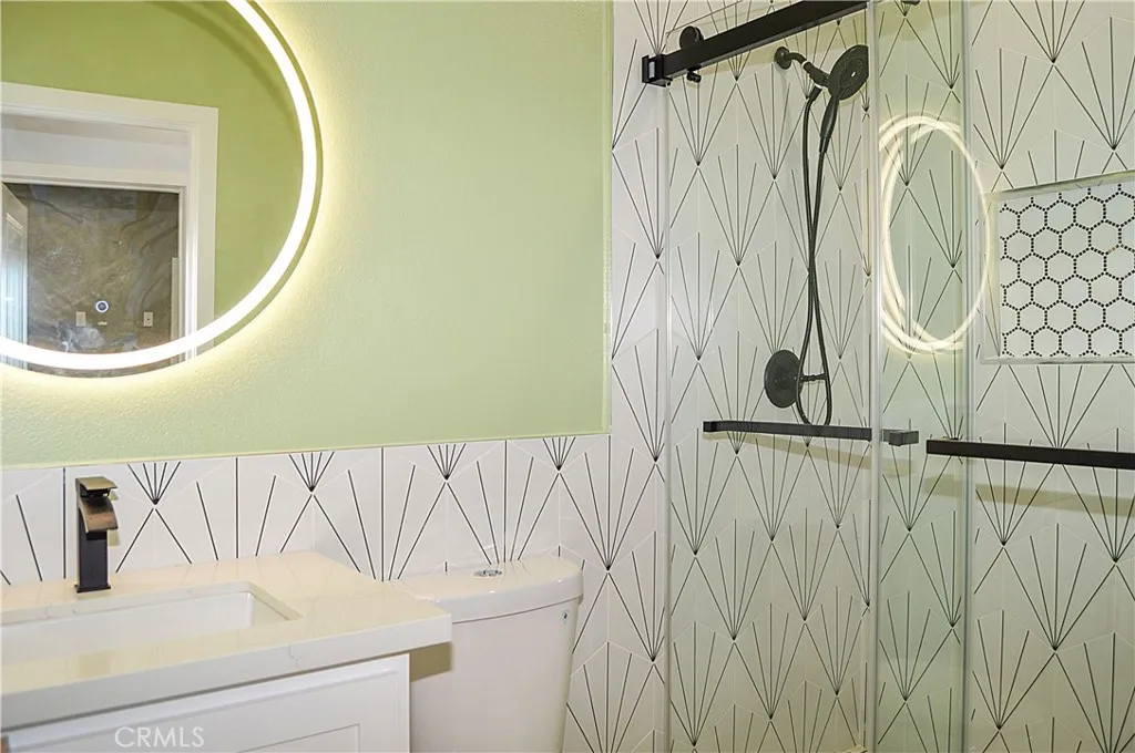 The 2nd upstairs bath sits across and adjacent to the 2nd and 3rd bedrooms and offers a custom tile surround for the easy-access shower with sliding glass doors, a lighted mirror over the modern vanity, recessed lighting, and a dual-flush commode.