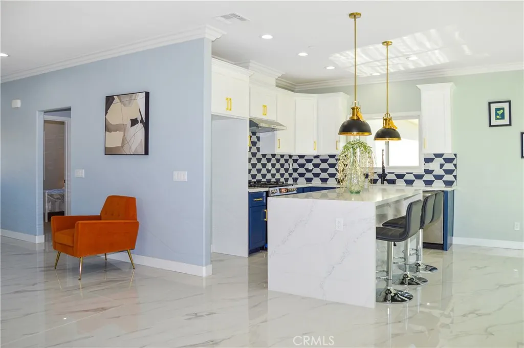 Gorgeous, modern kitchen with two-tone soft-close cabinetry with gold hardware, stainless steel appliances and sink, a quartz-topped breakfast bar with waterfall edges with pendant lighting above it, custom tile backsplash, and recessed lighting - all open to the great room and the views.