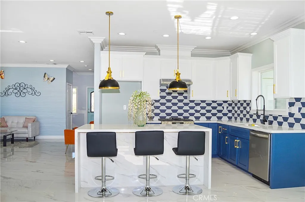 Gorgeous, modern kitchen with two-tone soft-close cabinetry with gold hardware, stainless steel appliances and sink, a quartz-topped breakfast bar with waterfall edges with pendant lighting above it, custom tile backsplash, and recessed lighting - all open to the great room and the views.
