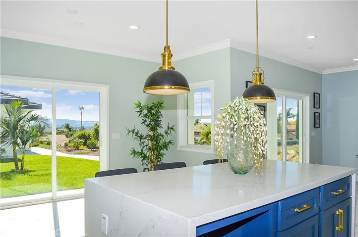 Gorgeous, modern kitchen with two-tone soft-close cabinetry with gold hardware, stainless steel appliances and sink, a quartz-topped breakfast bar with waterfall edges with pendant lighting above it, custom tile backsplash, and recessed lighting - all open to the great room and the views.