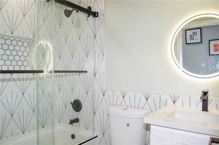 This stunning main floor bath sits across from the 4th bedroom and offers a custom tile surround for the shower/tub combo with sliding glass doors, a lighted mirror over the modern vanity, recessed lighting, tile flooring, and a dual-flush commode.