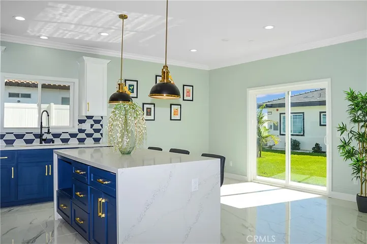 Gorgeous, modern kitchen with two-tone soft-close cabinetry with gold hardware, stainless steel appliances and sink, a quartz-topped breakfast bar with waterfall edges with pendant lighting above it, custom tile backsplash, and recessed lighting - all open to the great room and the views.