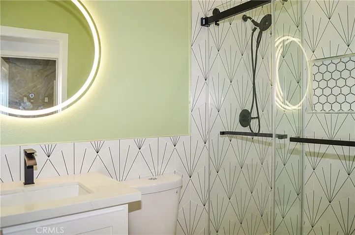 The 2nd upstairs bath sits across and adjacent to the 2nd and 3rd bedrooms and offers a custom tile surround for the easy-access shower with sliding glass doors, a lighted mirror over the modern vanity, recessed lighting, and a dual-flush commode.