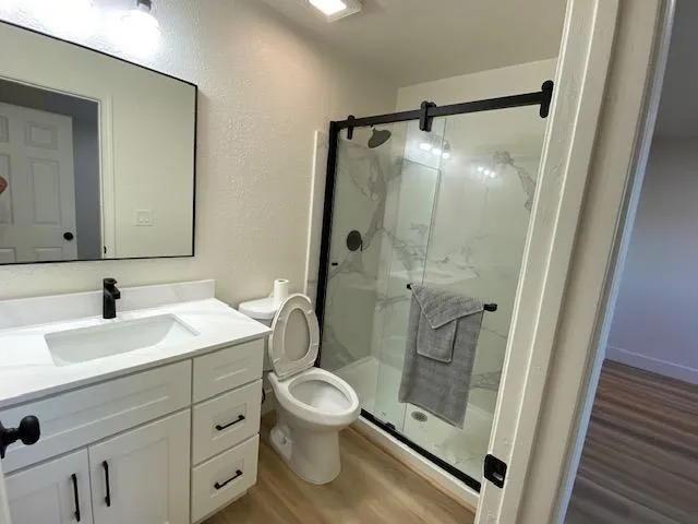 Bathroom with light wood-type flooring, vanity, a marble finish shower, and a textured wall