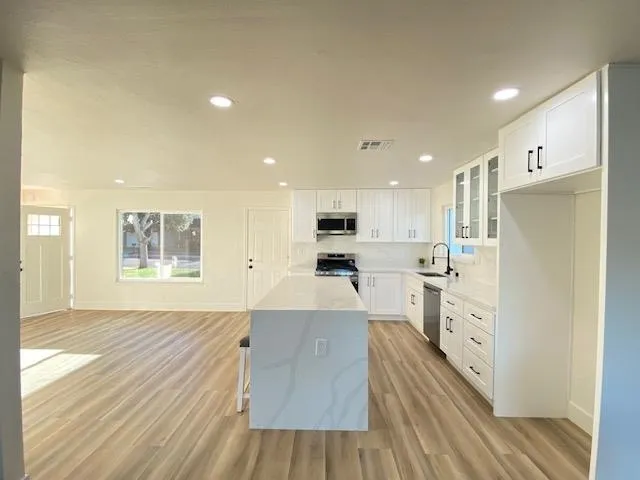 Kitchen with glass insert cabinets, white cabinets, a breakfast bar, light wood-style floors, and stainless steel appliances