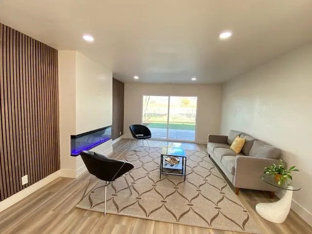 Living area featuring light wood-style flooring, a glass covered fireplace, and recessed lighting