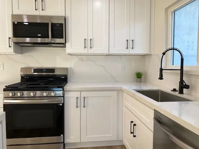Kitchen with stainless steel appliances, white cabinetry, and light stone counters