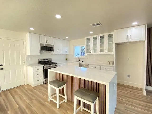 Kitchen featuring glass insert cabinets, a kitchen bar, appliances with stainless steel finishes, white cabinetry, and recessed lighting