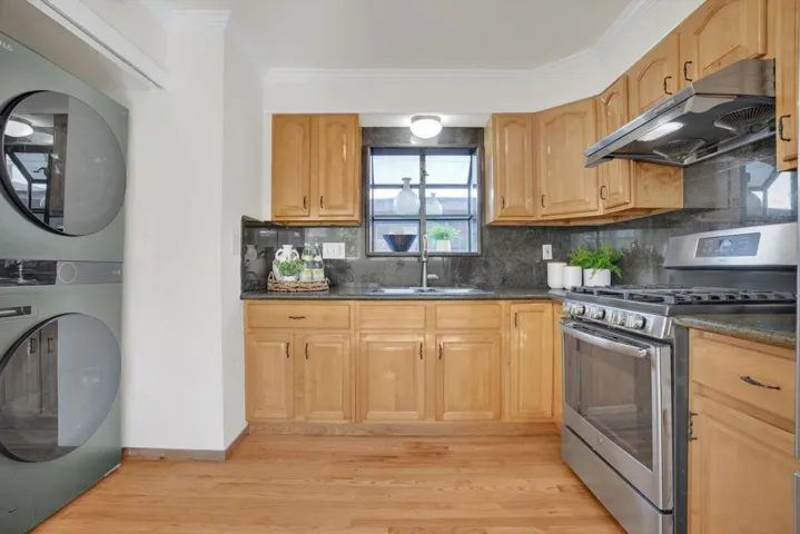 Kitchen with gas range, decorative backsplash, ventilation hood, stacked washing machine and dryer, and ornamental molding