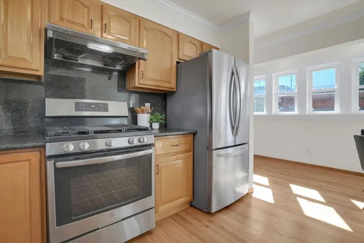 Kitchen featuring stainless steel appliances, tasteful backsplash, range hood, light wood-style floors, and ornamental molding