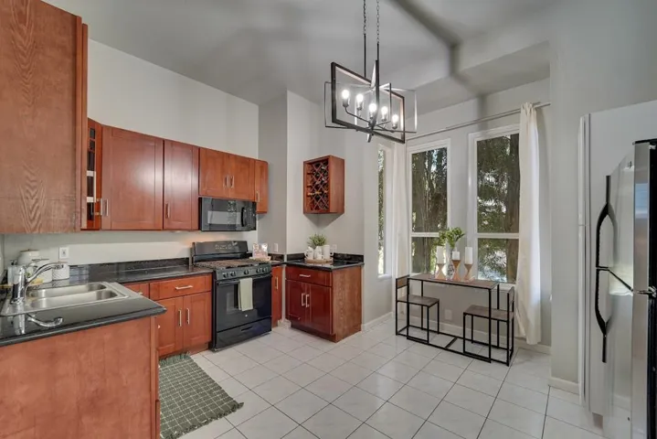 Kitchen with black appliances, decorative light fixtures, brown cabinets, and light tile patterned floors