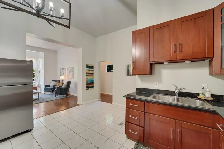 Kitchen with freestanding refrigerator, light tile patterned flooring, dark stone counters, brown cabinets, and open floor plan
