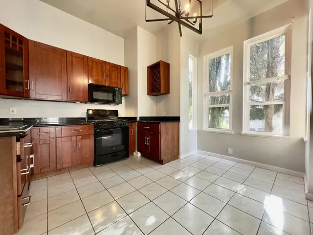 Kitchen with black appliances, light tile patterned floors, a chandelier, glass insert cabinets, and dark stone countertops