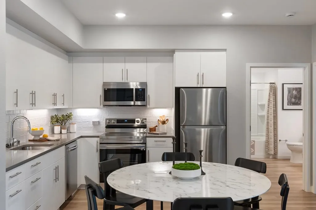 Kitchen featuring appliances with stainless steel finishes, backsplash, light wood-style flooring, white cabinetry, and dark stone counters