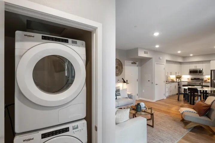 Laundry area with light wood-style flooring, estacked washer and dryer, and recessed lighting
