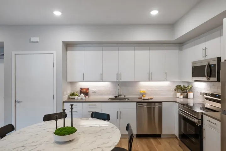 Kitchen with appliances with stainless steel finishes, white cabinets, light wood-type flooring, backsplash, and recessed lighting