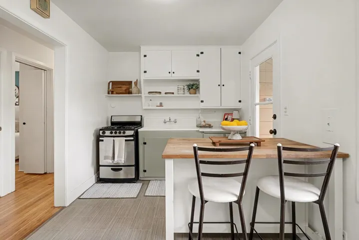 Kitchen featuring stainless steel gas range oven, a kitchen breakfast bar, white cabinets, and open shelves