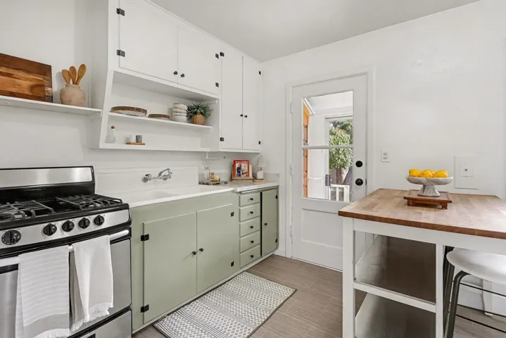 Kitchen featuring stainless steel gas range oven, open shelves, green cabinets, and white cabinets