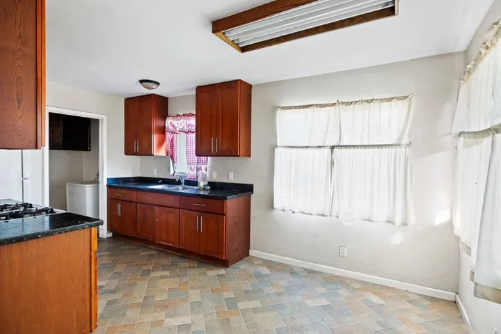 Kitchen with dark countertops, stone finish floors, freestanding refrigerator, and brown cabinetry