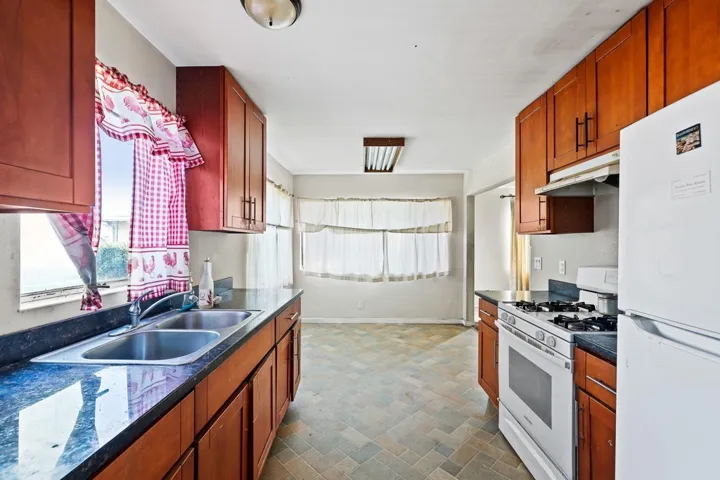 Kitchen featuring white appliances, under cabinet range hood, and brown cabinets