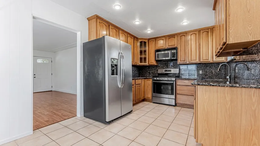 Kitchen with light tile patterned floors, stainless steel appliances, dark stone countertops, glass fronted cabinets, and backsplash