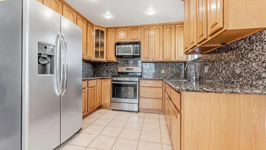 Kitchen with stainless steel appliances, dark stone counters, light tile patterned floors, and glass insert cabinets