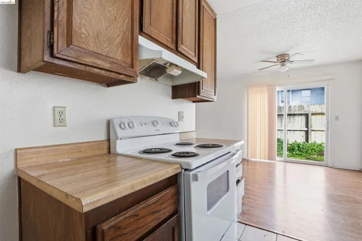 Kitchen featuring white electric range oven, light countertops, ceiling fan, a textured ceiling, and wood finish cabinetry