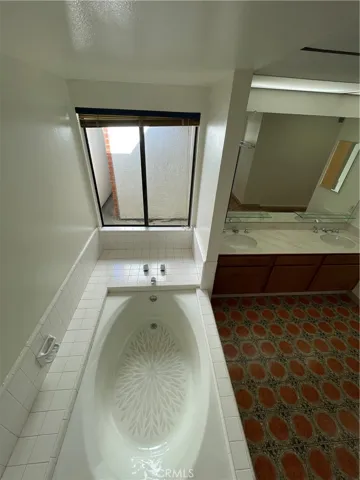 Top-down view of the bath tub, tile, and dual sink in the full bathroom
