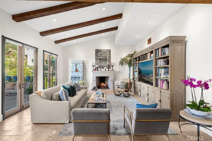 The main level showcases a spectacular great room with priceless ocean views, where a fireplace-warmed living area with wood-beamed vaulted ceilings, multi-paned windows, and French doors creates a light-filled, airy ambiance.