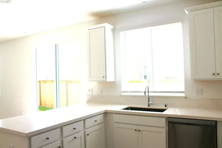 Kitchen with a peninsula, dishwashing machine, light countertops, and white cabinetry