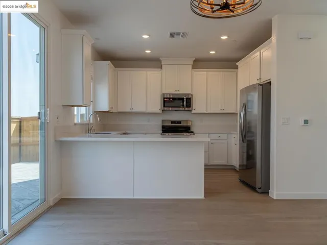 Kitchen with a peninsula, stainless steel appliances, light wood-style floors, light countertops, and recessed lighting