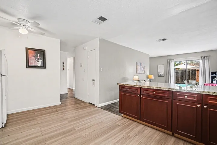 Kitchen with dark brown cabinets, light stone counters, light wood-type flooring, freestanding refrigerator, and a textured ceiling