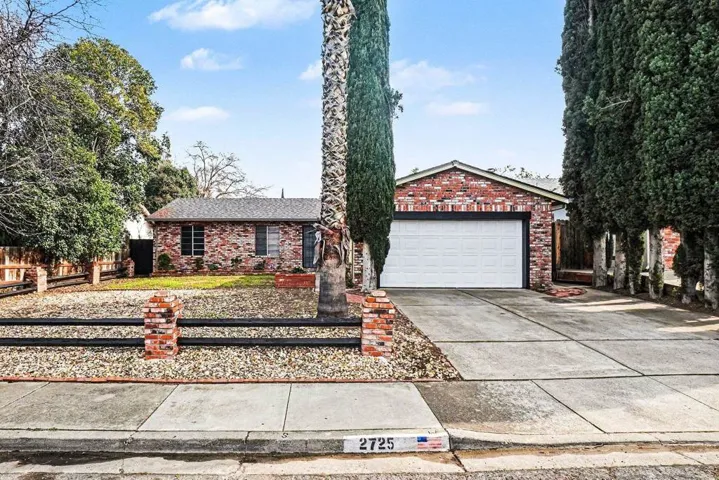 Single story home with driveway, brick siding, and roof with shingles