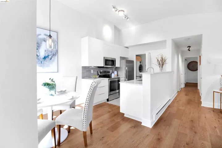 Kitchen with stainless steel appliances, modern cabinets, white cabinets, baseboard heating, and light wood finished floors