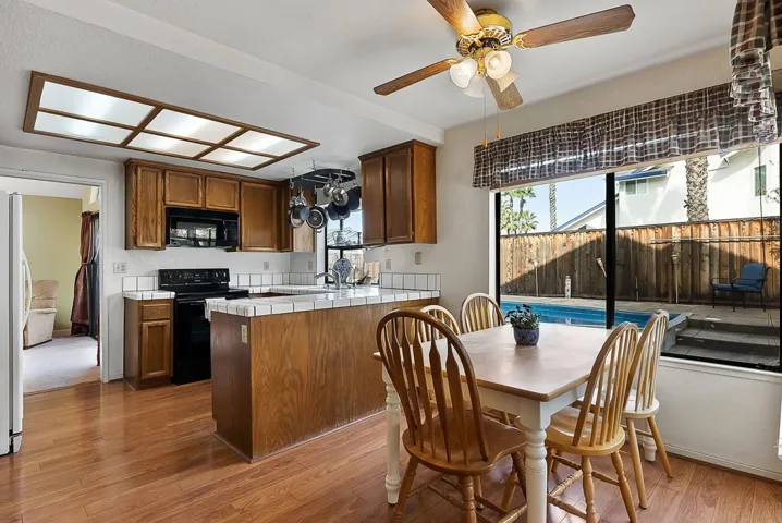 Kitchen with tile countertops, black appliances, dark wood-style flooring, ceiling fan, and wood finish cabinets