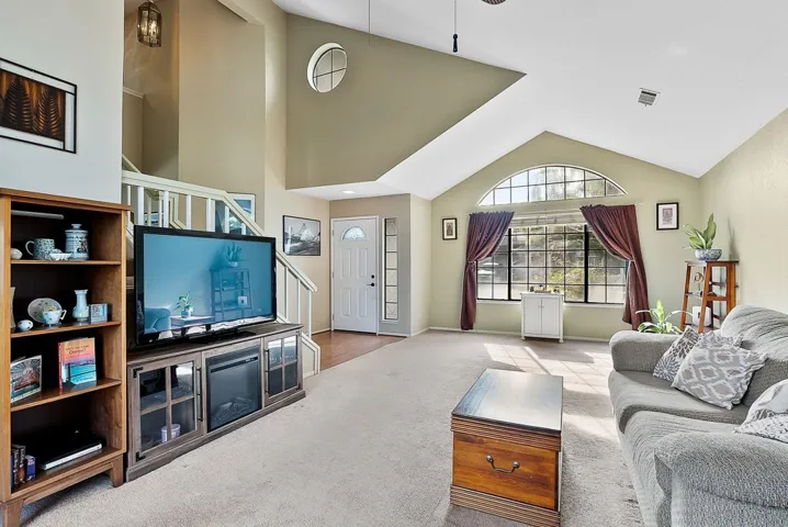 Carpeted living area featuring stairway and vaulted ceiling