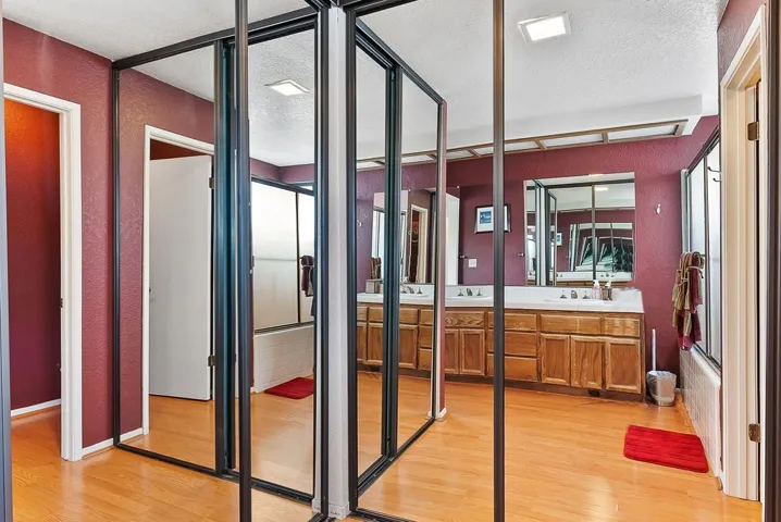 Full bathroom featuring vanity, a textured ceiling, light wood finished floors, combined bath / shower with glass door, and a textured wall