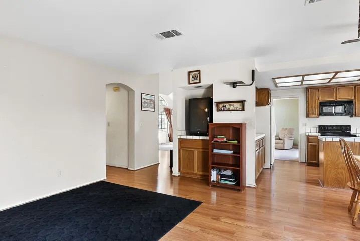 Kitchen featuring tile counters, wood finish cabinetry, arched walkways, and light wood-type flooring