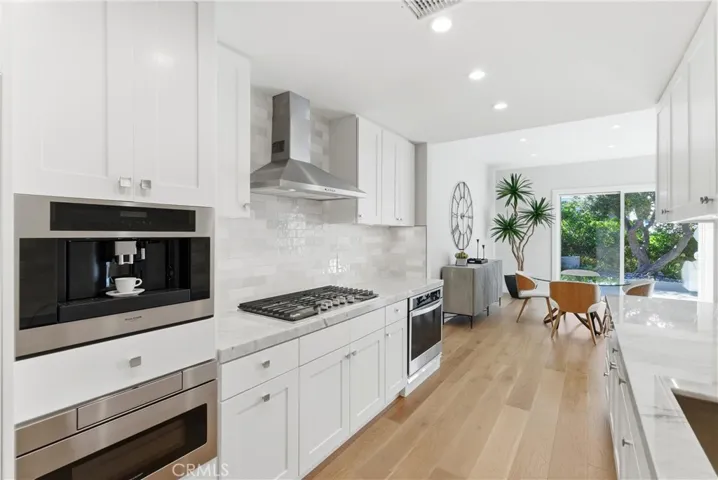 Modern kitchen featuring white shaker cabinetry, marble-style counters, stainless appliances, gas cooktop, and a built-in Fulgor Milano coffee machine, opening to a bright dining area with seamless indoor-outdoor flow.
