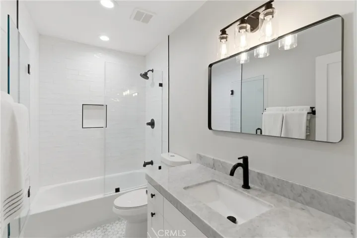 Beautifully updated secondary bathroom featuring marble countertops, a sleek vanity with modern fixtures, and a tub and shower combination with clean, contemporary tile finishes for a bright, spa-like feel.