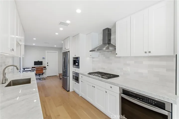 Beautifully updated kitchen featuring white shaker cabinetry, marble countertops, stainless steel appliances, and ample storage.